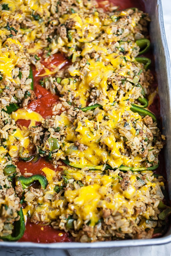 Cooked halved poblano peppers with filling, sauce, and melted cheese in metal cake pan.