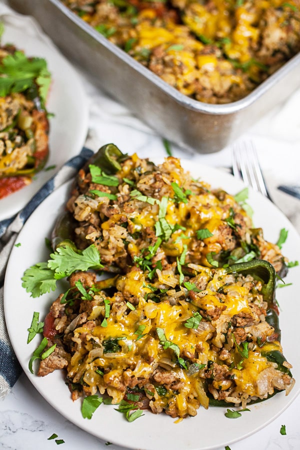 Stuffed poblano peppers with ground turkey, rice, and cheese on small white plates.