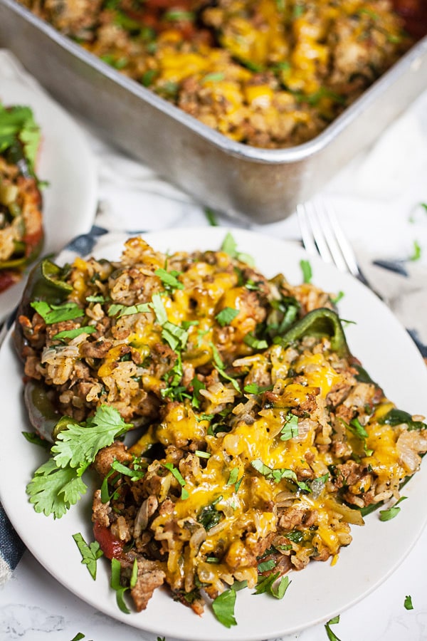 Stuffed poblano peppers with filling, cheese, and minced cilantro on white plates in front of cake pan.