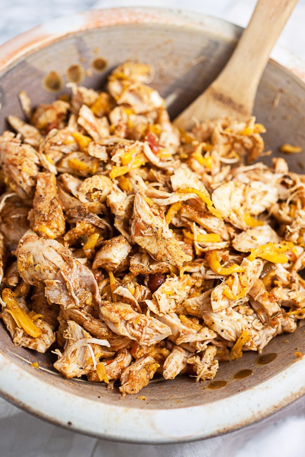 Shredded chicken and cheese in ceramic bowl with wooden spoon.