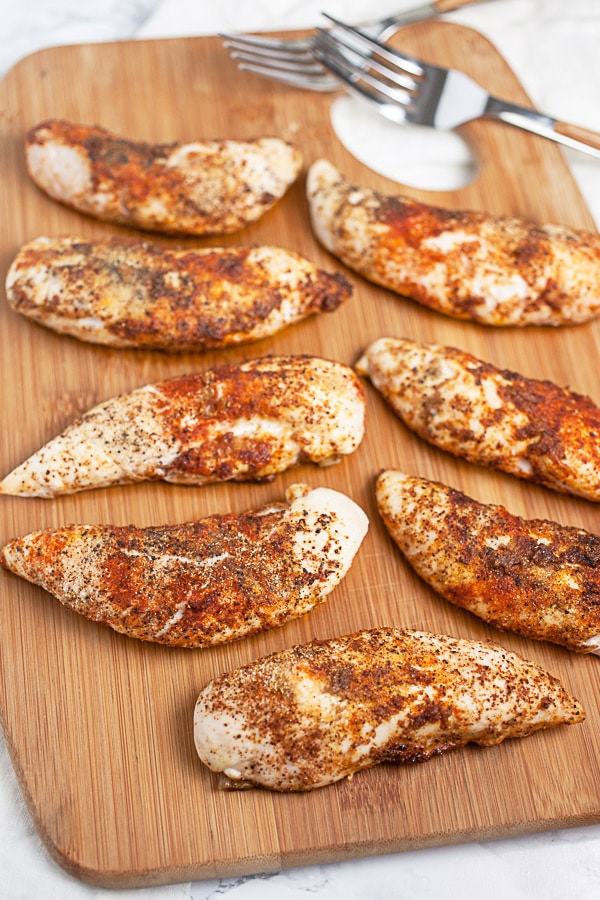 Baked chicken tenderloins on wooden cutting board.