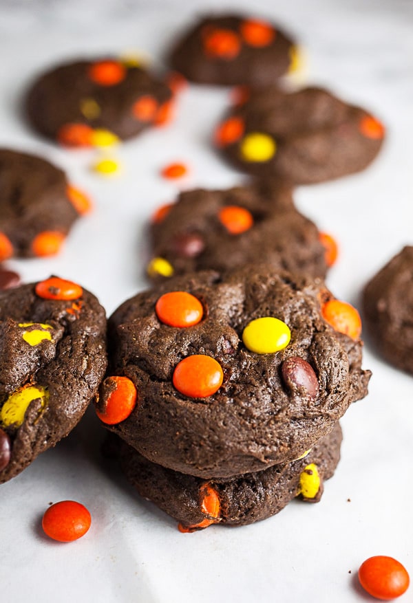 Reese's Pieces chocolate cookies stacked on white surface.