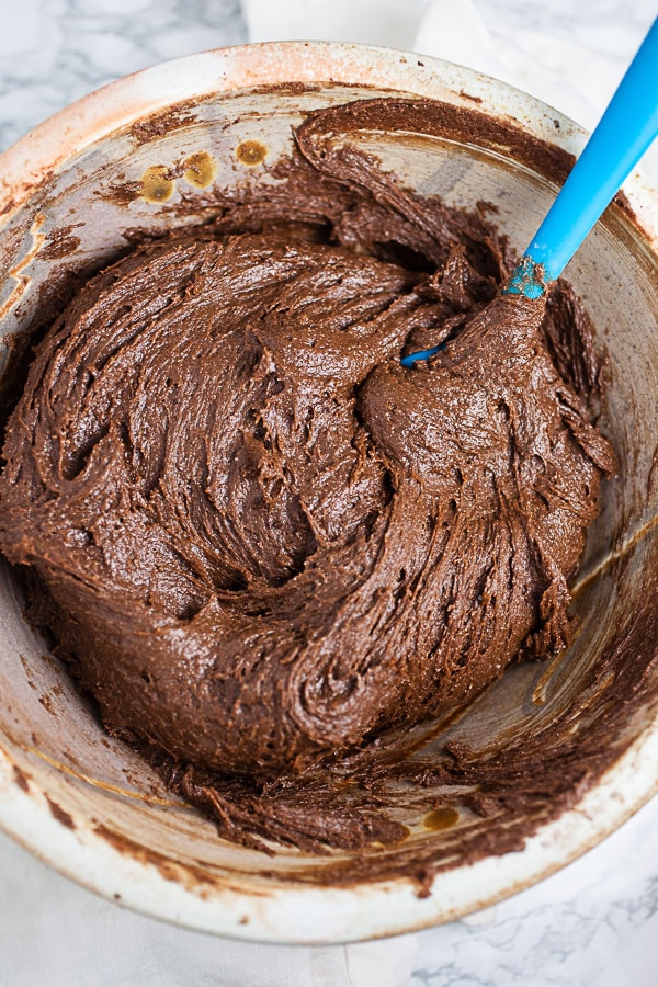 Chocolate cookie batter in ceramic bowl with blue spatula.