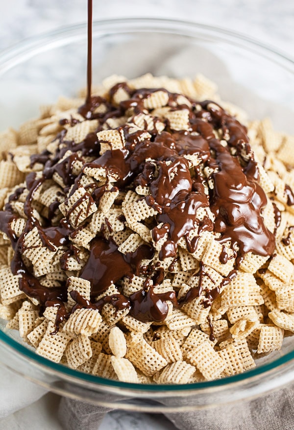 Melted chocolate peanut butter mixture drizzled onto rice Chex in large glass bowl.