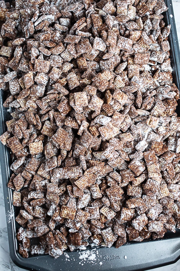 Puppy chow tossed with powdered sugar on metal baking sheet.