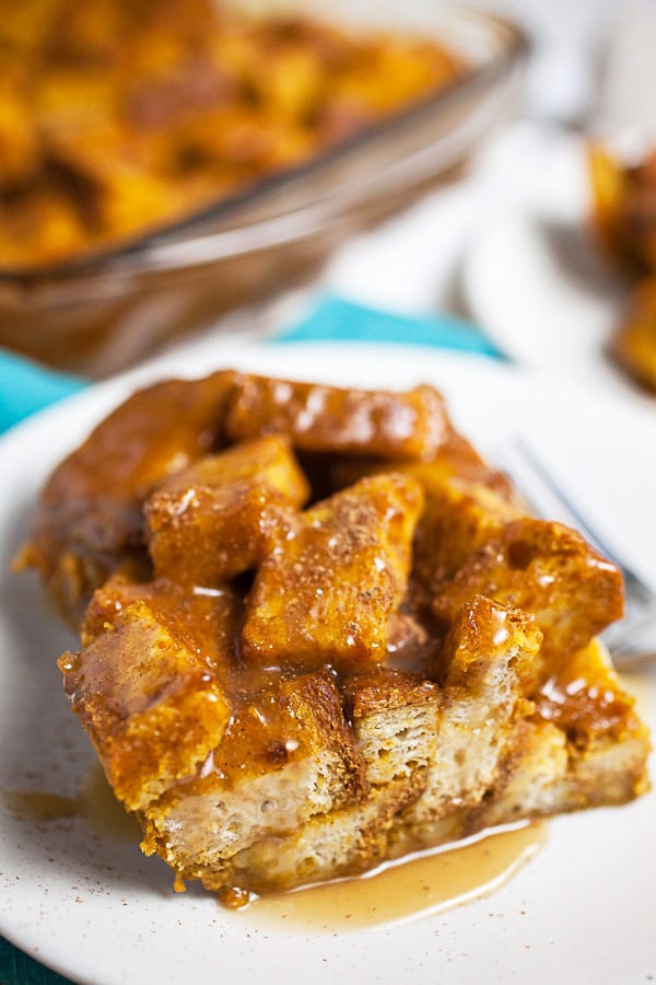 Pumpkin bread pudding on small white plates topped with caramel sauce.