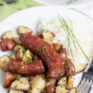 Sheet pan sausage and potatoes on white plate with sauerkraut.