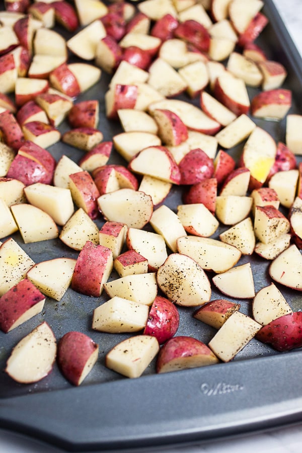 Uncooked diced red potatoes tossed in olive oil on metal baking sheet.