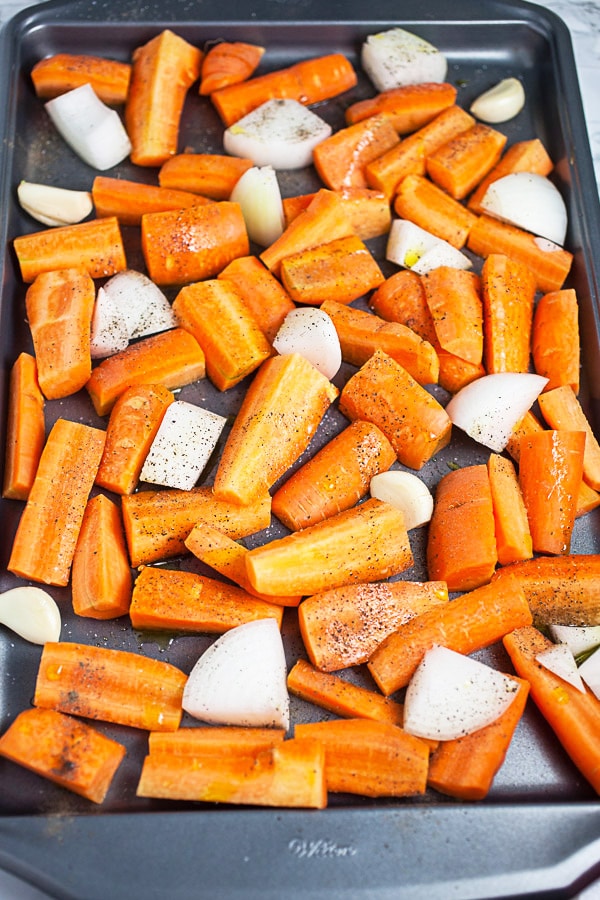 Carrot chunks, onions, and garlic cloves on metal baking sheet.