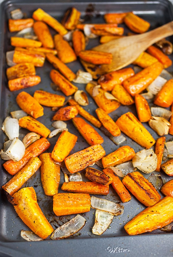 Roasted carrots, onions, and garlic cloves on metal baking sheet.