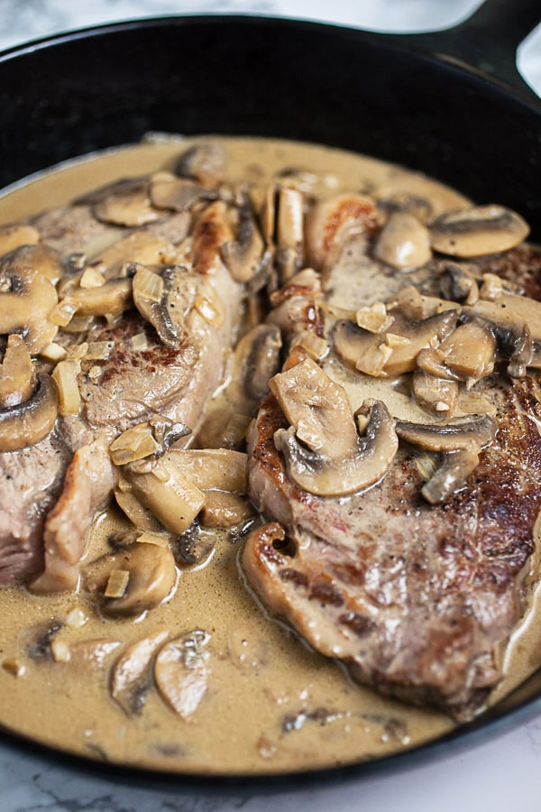 Cooked New York strip steaks and creamy mushroom sauce in cast iron skillet.