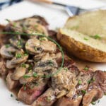 Sliced Steak Diane with mushroom sauce on white plate with baked potato.