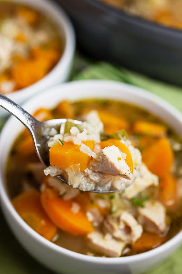 Spoonful of turkey rice soup lifted from white bowl.