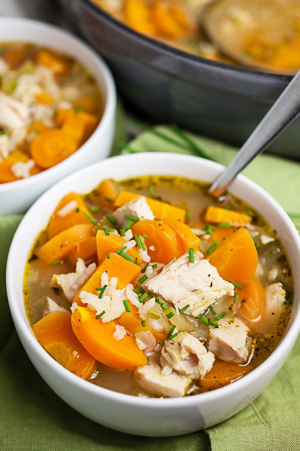 Turkey rice soup garnished with fresh chives in white bowls.