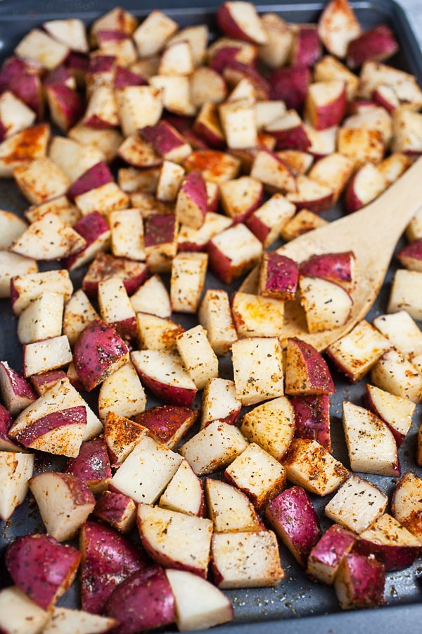 Uncooked diced potatoes tossed in olive oil and spices on baking sheet.