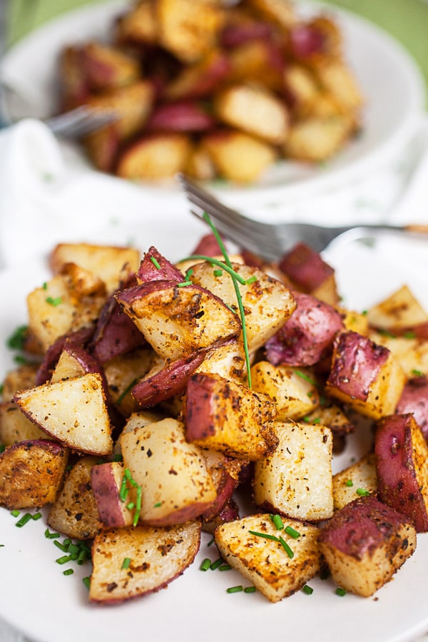 Roasted red potatoes garnished with fresh chives on small white plates.