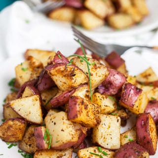 Roasted red potatoes on small white plates with forks.