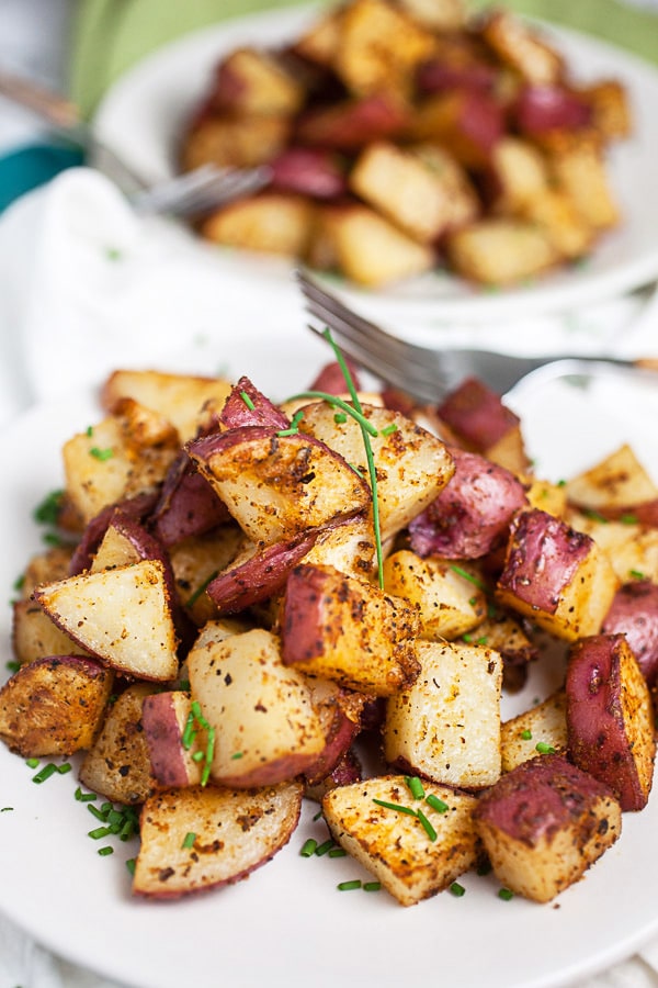 Roasted red potatoes on small white plates with forks.