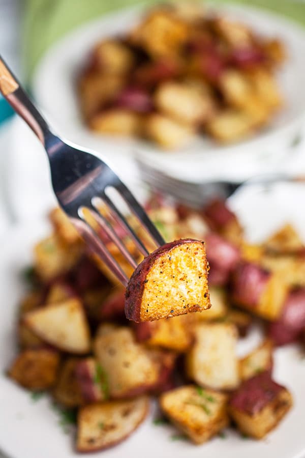 Fork holding roasted potato lifted from white plate.