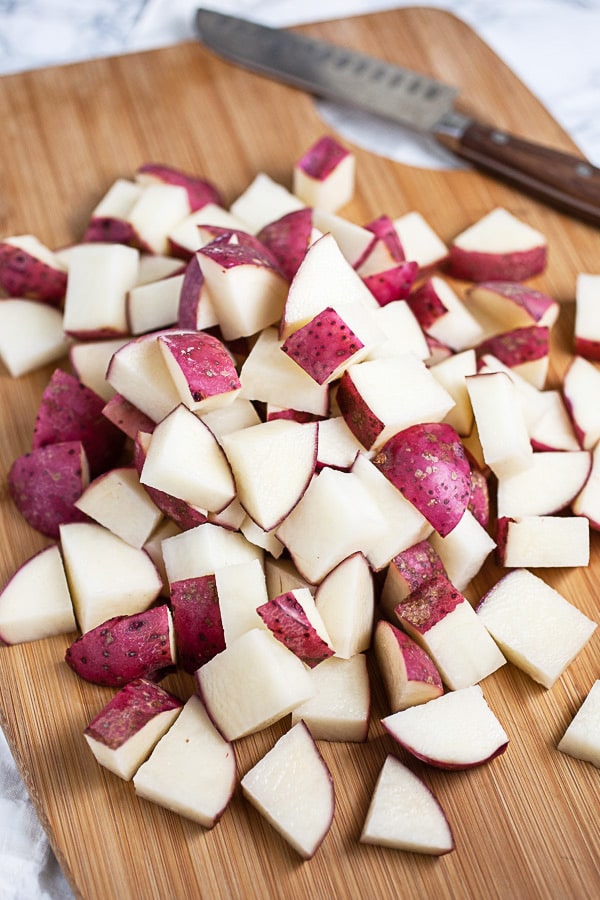 Diced red potatoes on wooden cutting board with knife.