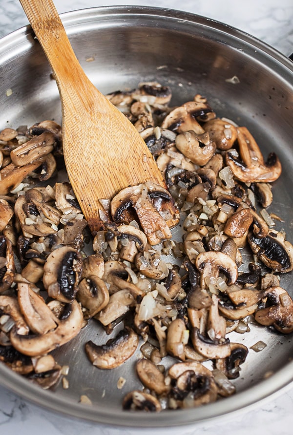 Sautéed mushrooms and shallots in skillet with wooden spatula.
