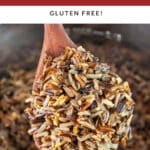 Cooked wild rice lifted from Instant Pot on wooden spoon.