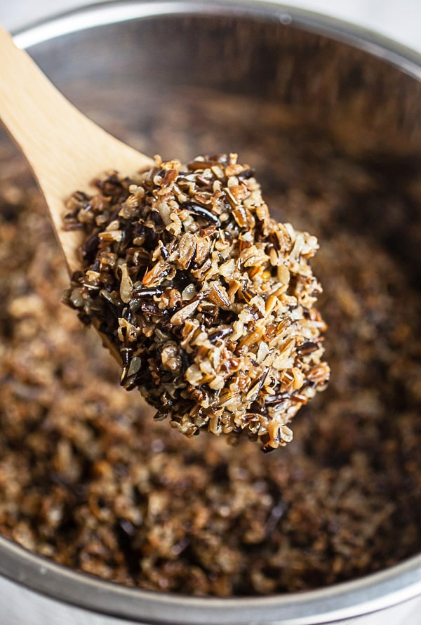 Scoop of cooked wild rice lifted from Instant Pot on wooden spoon.