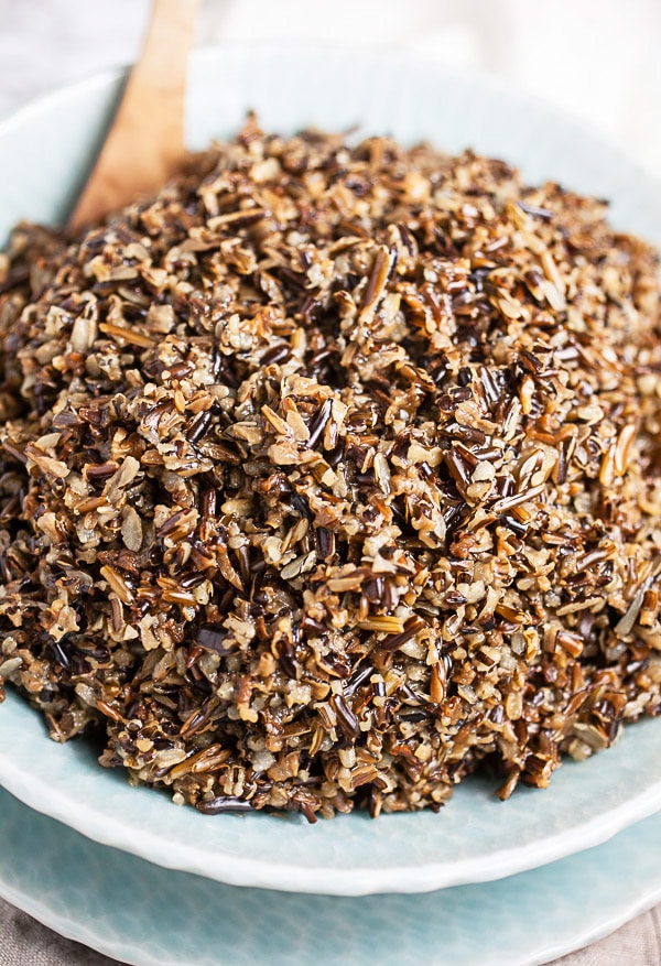 Cooked wild rice in blue serving bowl with wooden spoon.