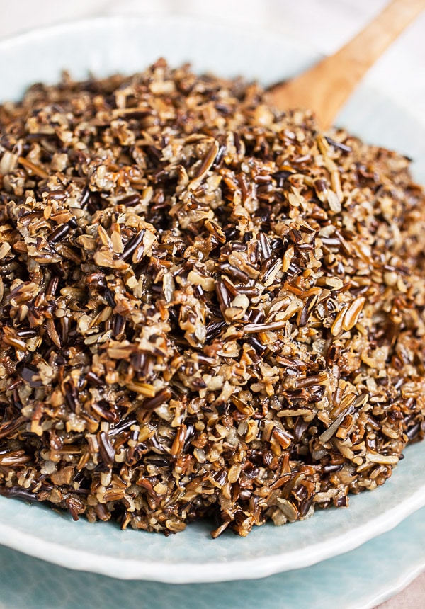 Cooked wild rice in blue serving bowl with wooden spoon.