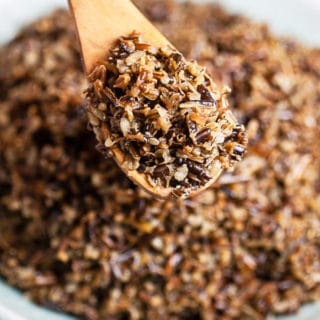 Cooked wild rice lifted from serving bowl on wooden spoon.