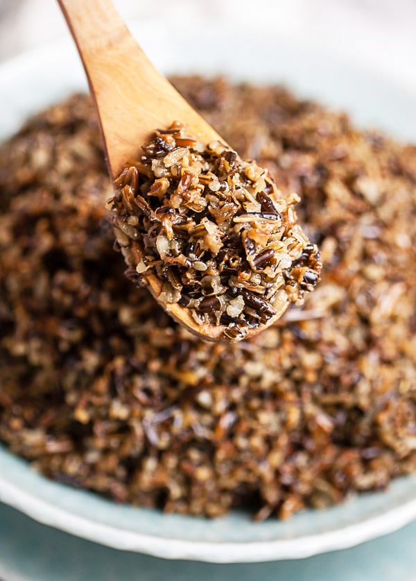 Cooked wild rice lifted from serving bowl on wooden spoon.