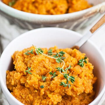 Mashed sweet potatoes with thyme in white bowl with fork.