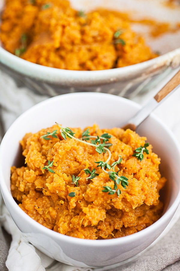 Mashed sweet potatoes with thyme in white bowl with fork.