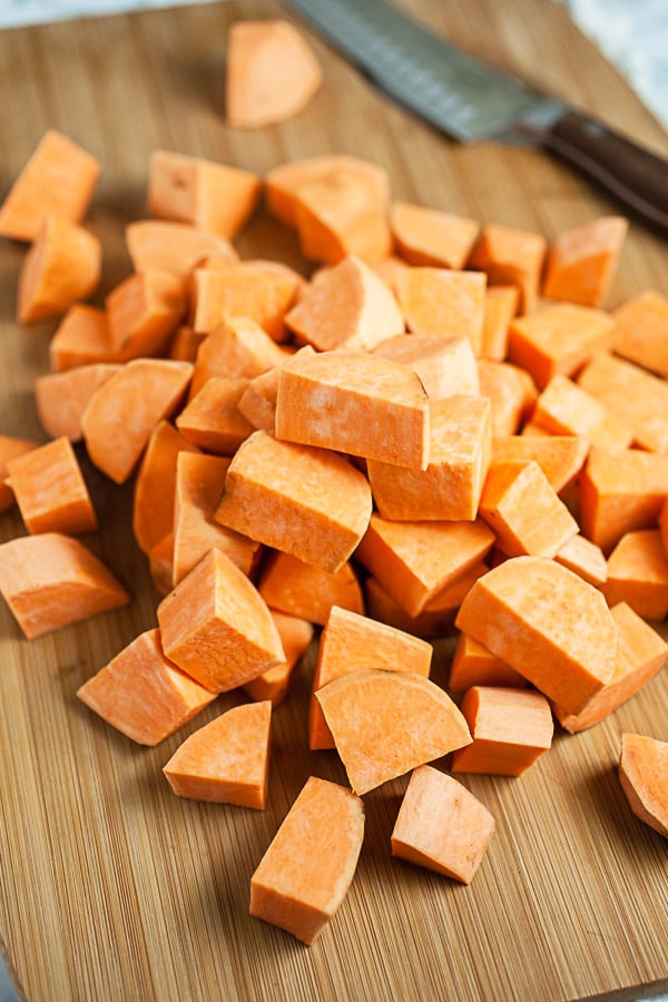 Diced sweet potatoes on wooden cutting board with knife.
