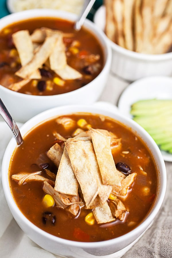 Chicken tortilla soup with corn tortilla strips in white bowls.