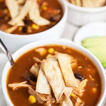 Chicken tortilla soup with corn tortilla strips in white bowls.