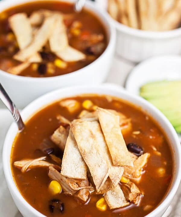 Chicken tortilla soup with corn tortilla strips in white bowls.