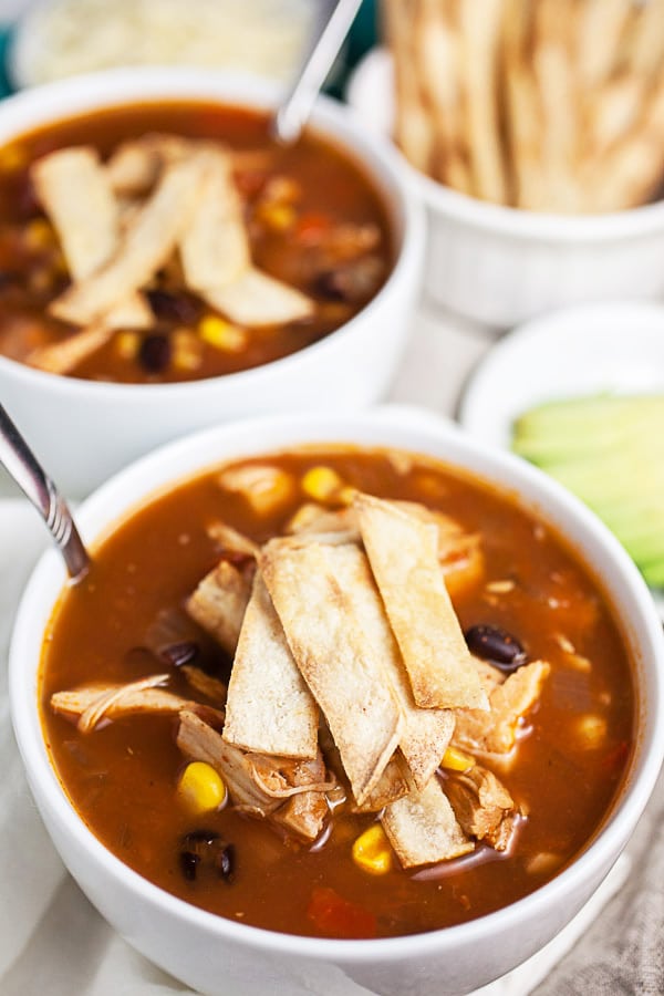 Chicken tortilla soup with corn tortilla strips in white bowls.