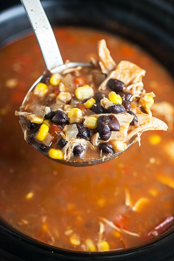 Scoop of chicken tortilla soup lifted from slow cooker on metal ladle.