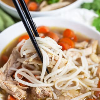 Chopsticks lifting rice noodles from bowl of Vietnamese chicken soup.