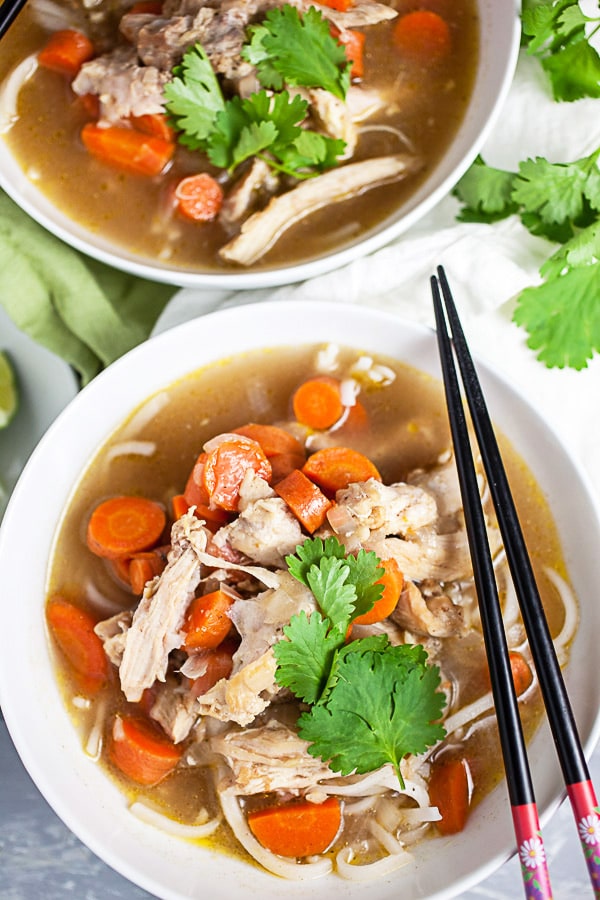 Chopsticks sitting on white bowl of Vietnamese chicken soup with cilantro.