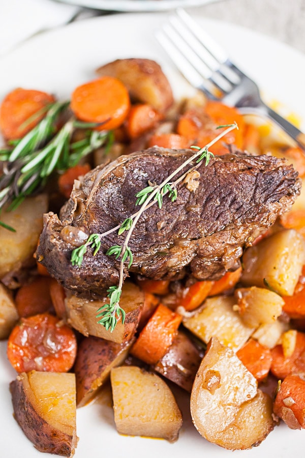 Red wine pot roast with herbs, potatoes, and carrots on white plate with fork.