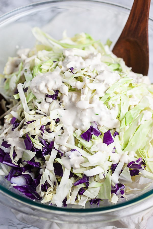 Shredded red and green cabbage topped with dressing in glass mixing bowl.