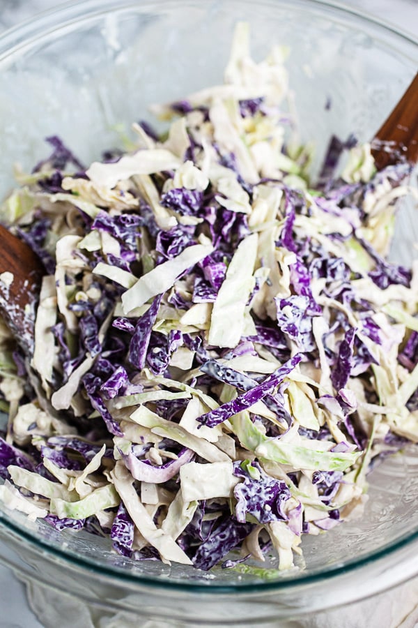 Red and green cabbage tossed with dressing in large glass mixing bowl.