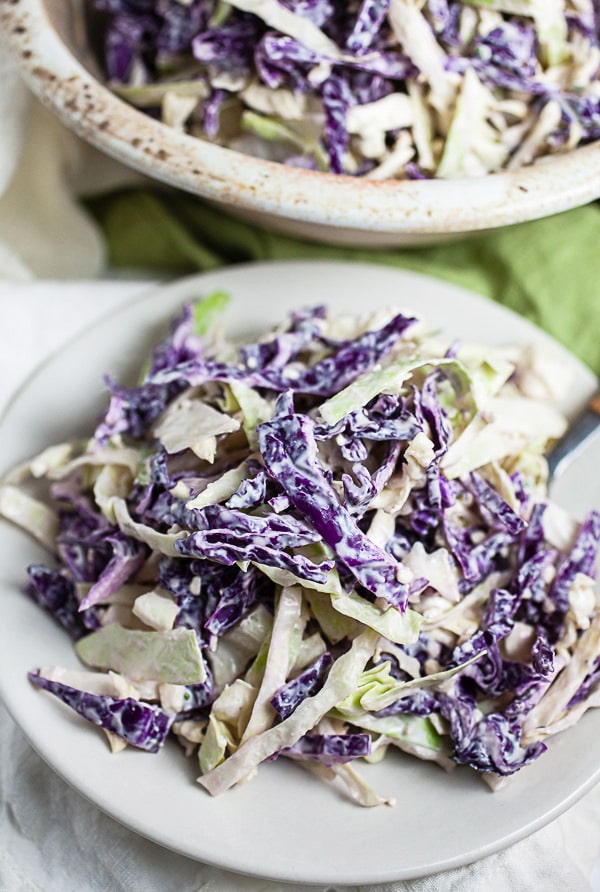 Blue cheese coleslaw on small white plate in front of ceramic bowl.