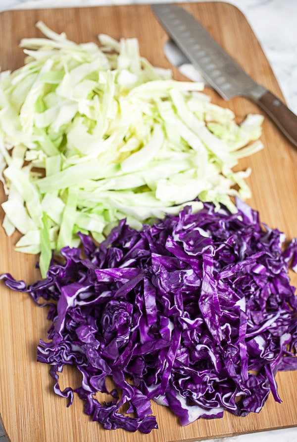 Sliced red and green cabbage on wooden cutting board with knife.