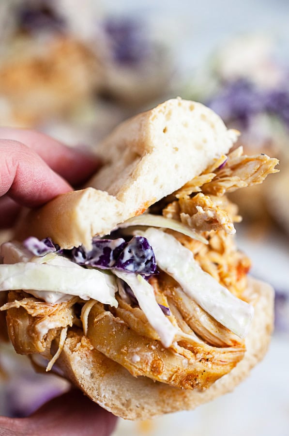 Hand holding shredded buffalo chicken sandwich with blue cheese coleslaw.
