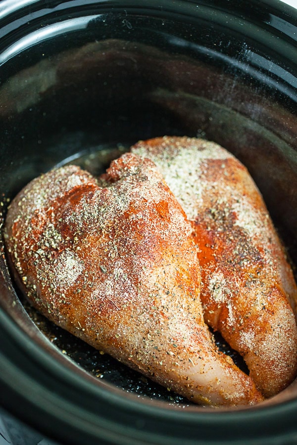 Raw chicken breasts with spices in crockpot.