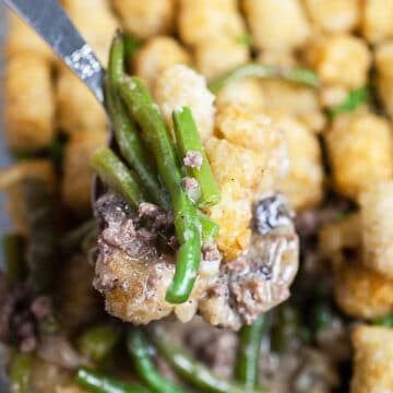 Scoop of tater tot hotdish lifted from glass baking pan.