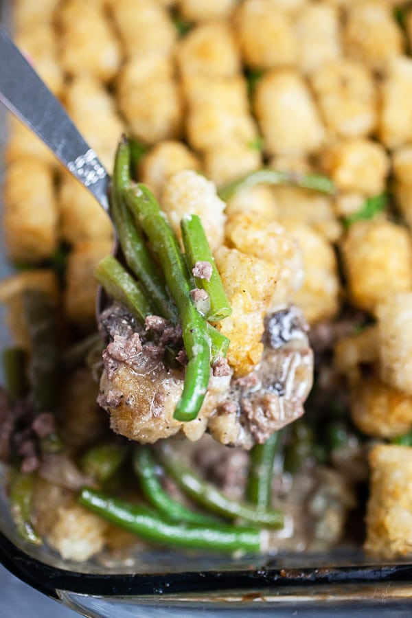 Scoop of tater tot hotdish lifted from glass baking pan.